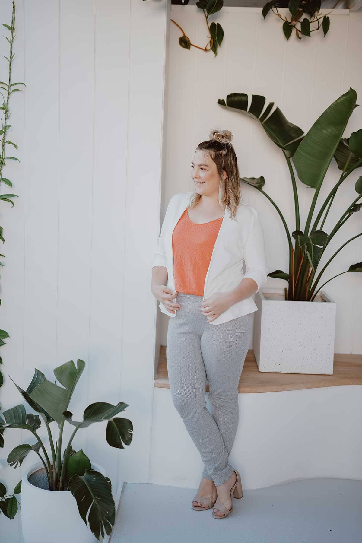 Administrator Krystal of Hubblit - wearing white suit jacket and peach top, white background and greenry full length shot