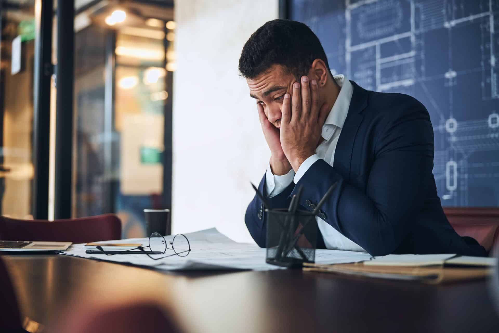 man in suit with hands on face looking stressed at paperwork