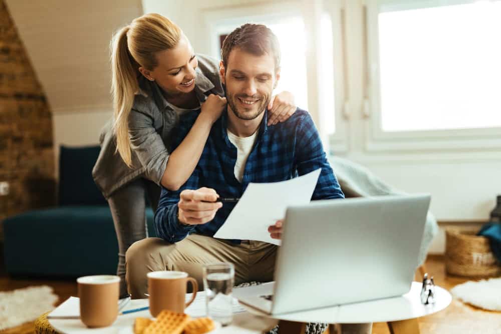 happy couple hugging looking over paperwork and computer